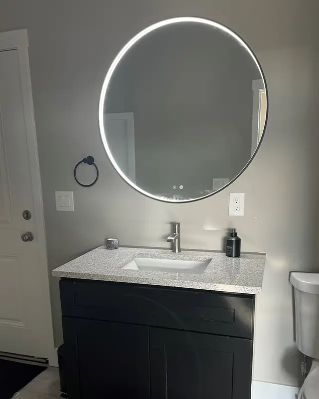 A backlit round LED mirror over a bathroom vanity