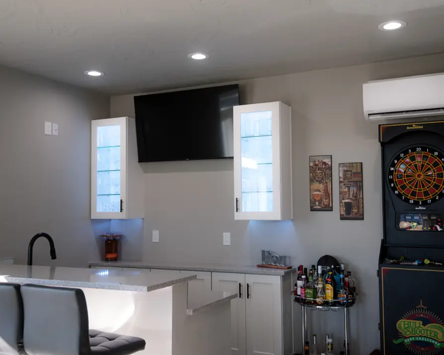 Bar wall with a mounted TV, lit glass cabinets and recessed lighting