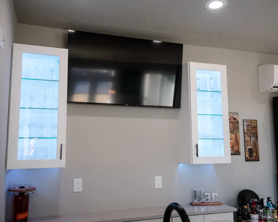 Close view of lit glass cabinets and under-cabinet light beside the wall TV
