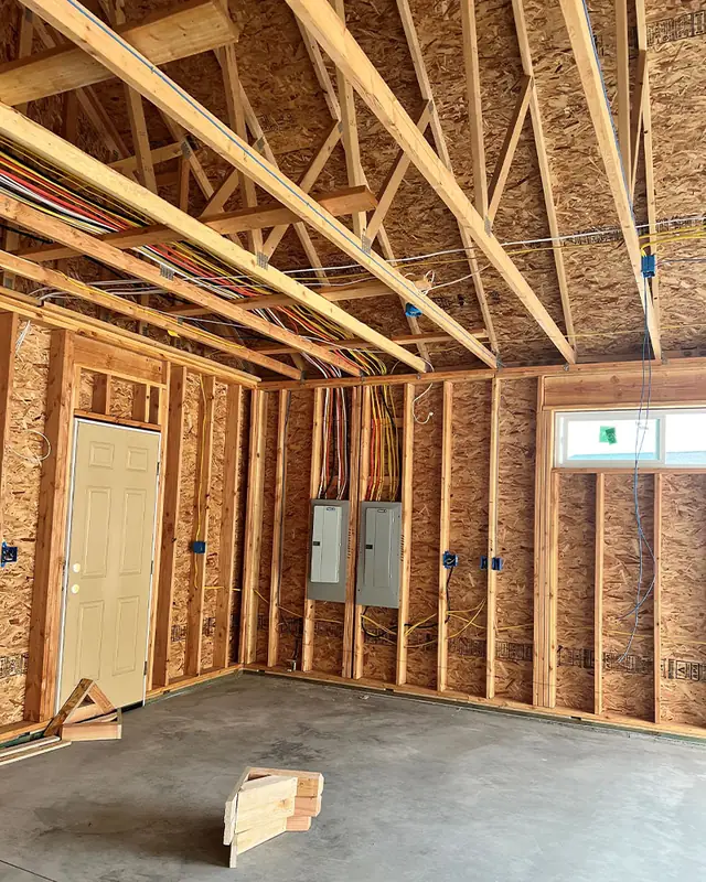 New-construction garage rough-in with two electrical panels and cable runs through the trusses