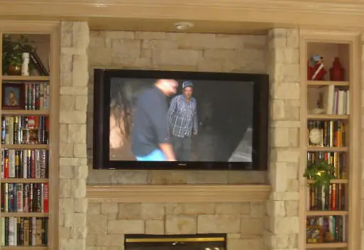 A TV mounted in a stone fireplace with bookshelves either side