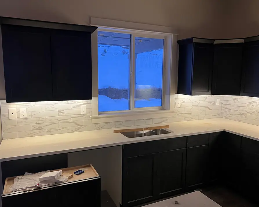 Navy kitchen cabinets with under-cabinet LED lighting over marble tile